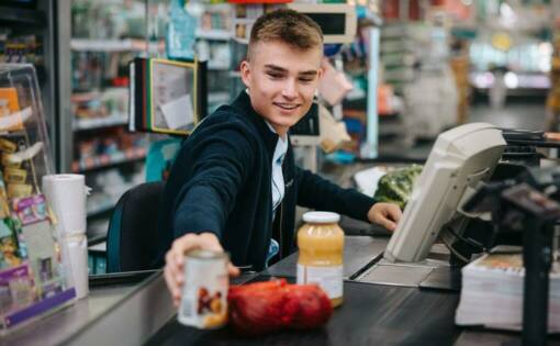A young employee scanning items at a supermarket register